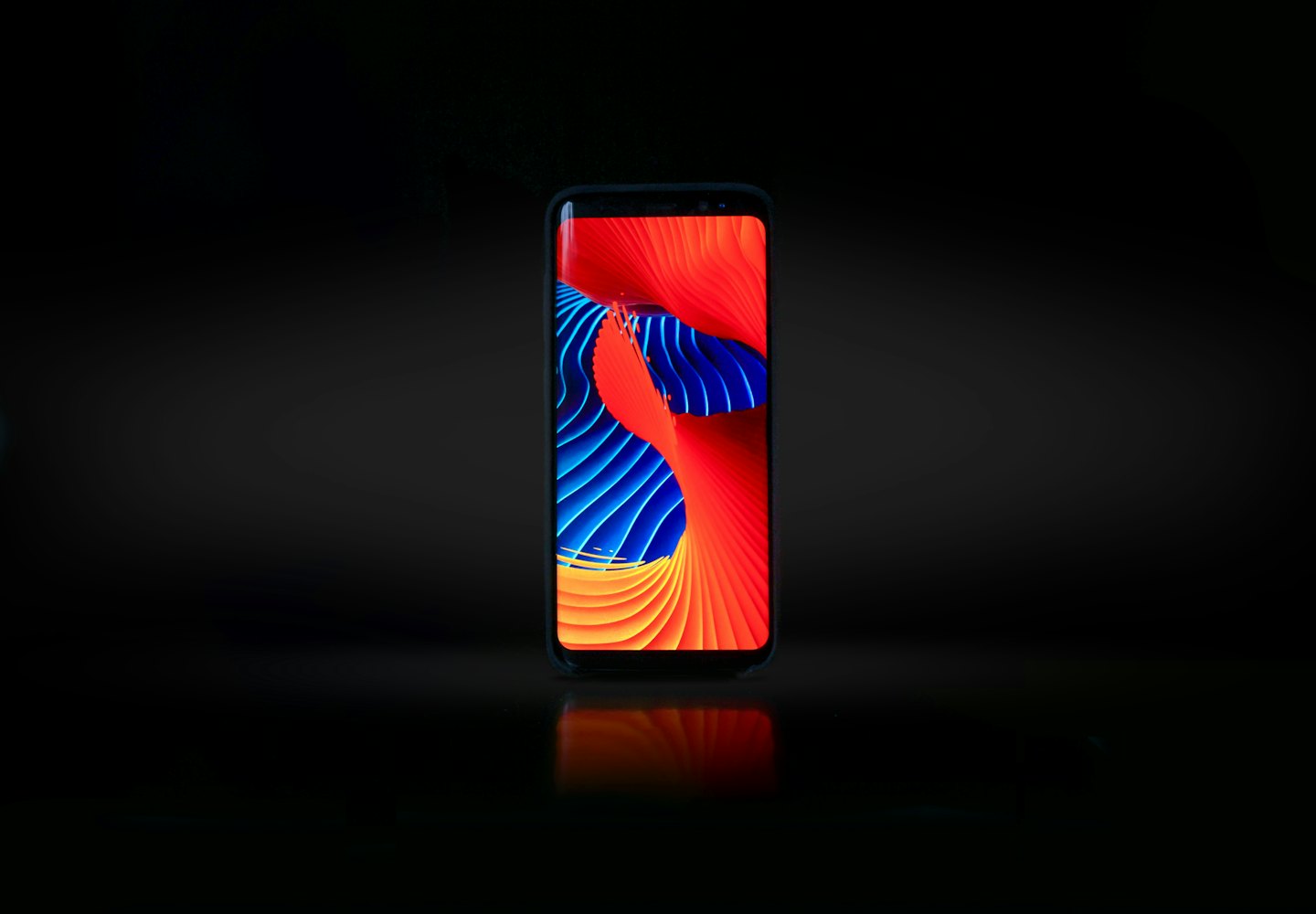 Smartphone displays vibrant abstract wallpaper on a dark reflective surface.