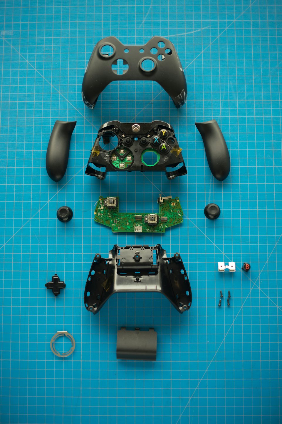 Disassembled Xbox controller parts on a blue grid mat.